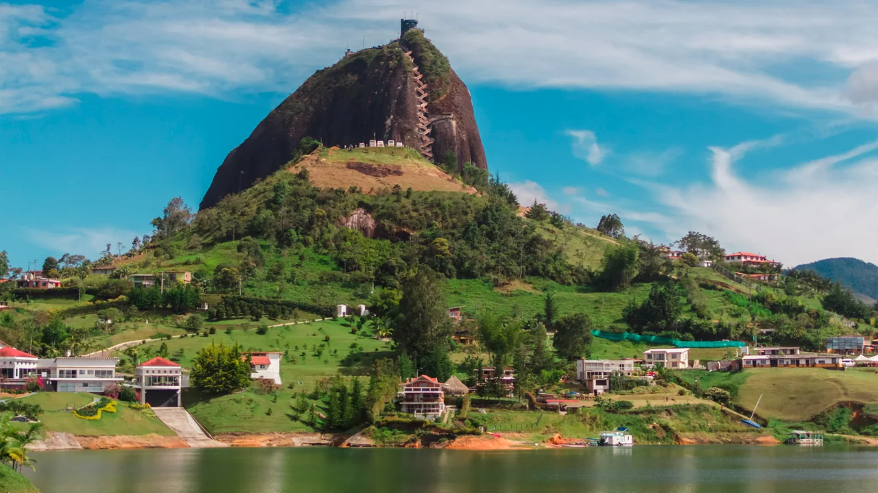 El Peñón de Guatapé, un monolito de piedra con su escalera tallada, rodeado de colinas verdes, casas de colores y el embalse.