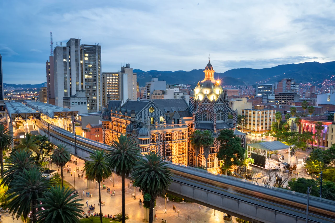 Centro de Medellín al anochecer: el Palacio de la Cultura iluminado, la línea del Metro y el skyline de la ciudad.